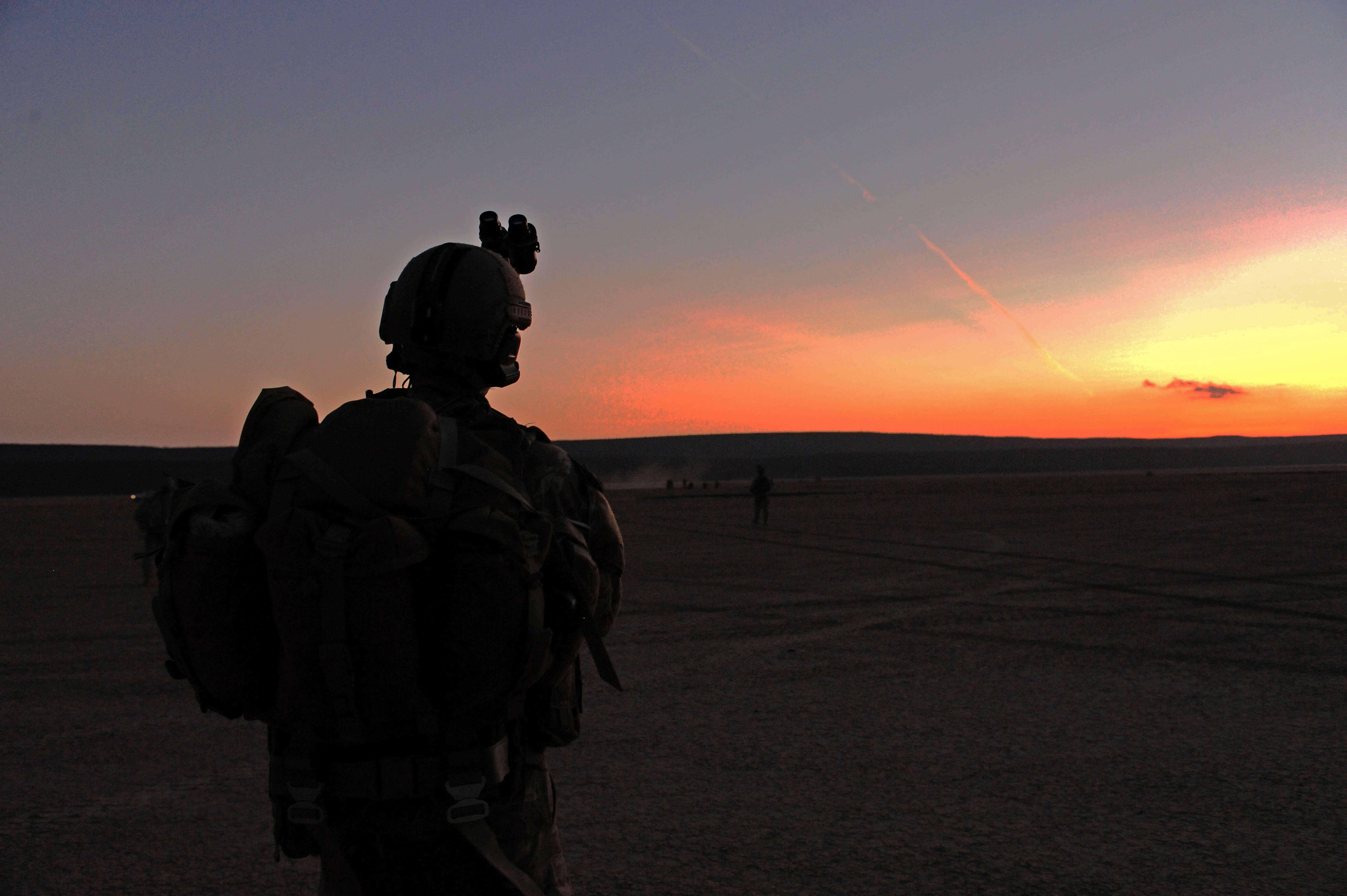 A soldier in full tacticle gear looking at the sunset in Afganistan