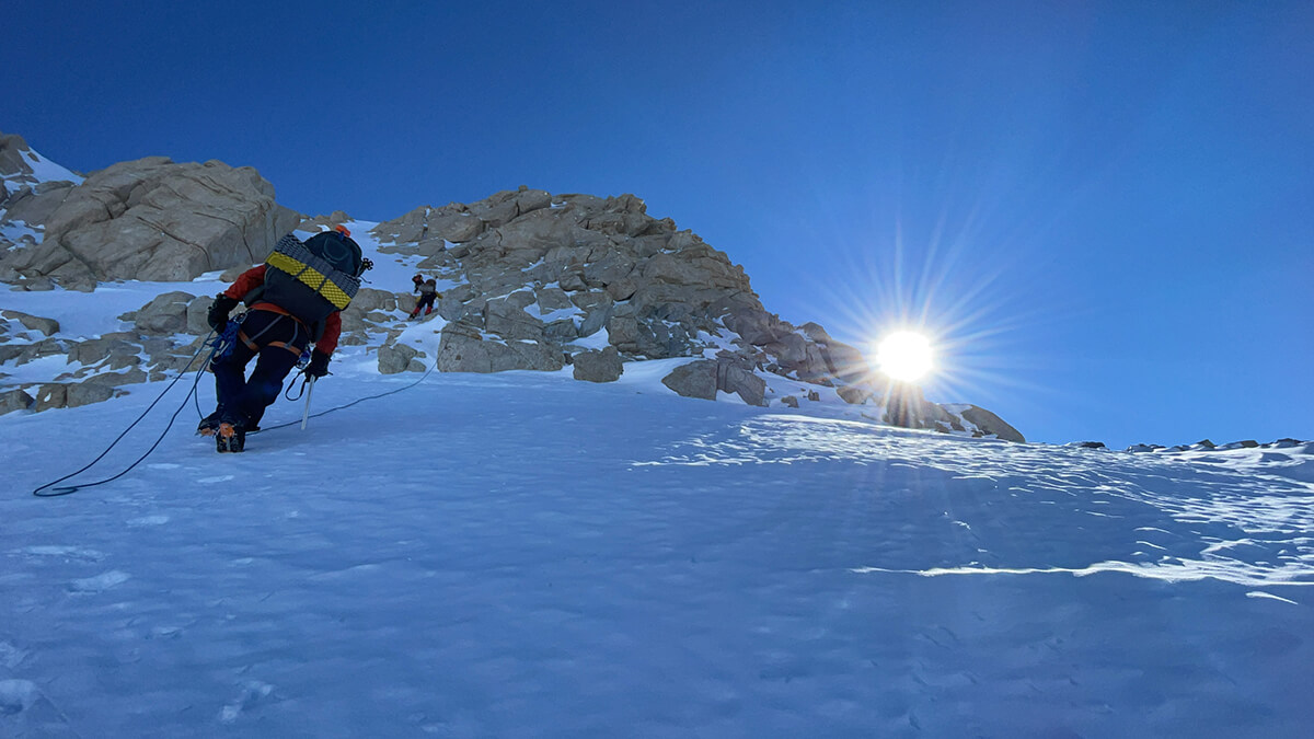 team member climbing mountain with sunrise